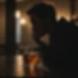 Silhouette of a person staring at a glass of whiskey in dim lighting